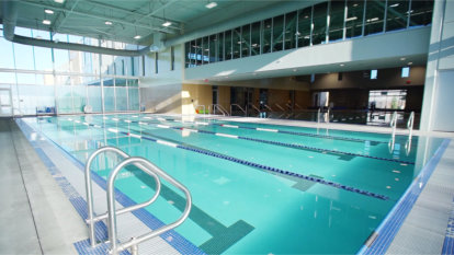 Fitness center's lap pool in the foreground, with glimpses of the walking track above and group exercise pool in the back.