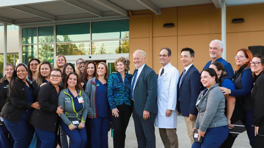 Providers and other care team members posing together with Heidi Y Campini in front of the Cancer Center entrance.